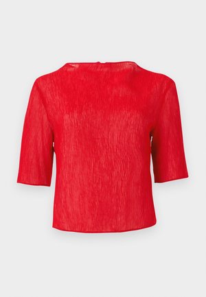 Blouse rouge texturée à manches courtes avec un col rond et une coupe légèrement ample sur un fond uni.