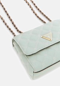 Gequilte lichtgroene handtas van imitatieleren met een gouden driehoekig logo, zwarte accenten en een kettingriem, met een diagonaal stikselpatroon.