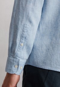 Lichtblauwe linnen shirt met een gestructureerde afwerking. Beschikt over twee knopenmanchetten, een subtiel getailleerde pasvorm en een button-down kraag.