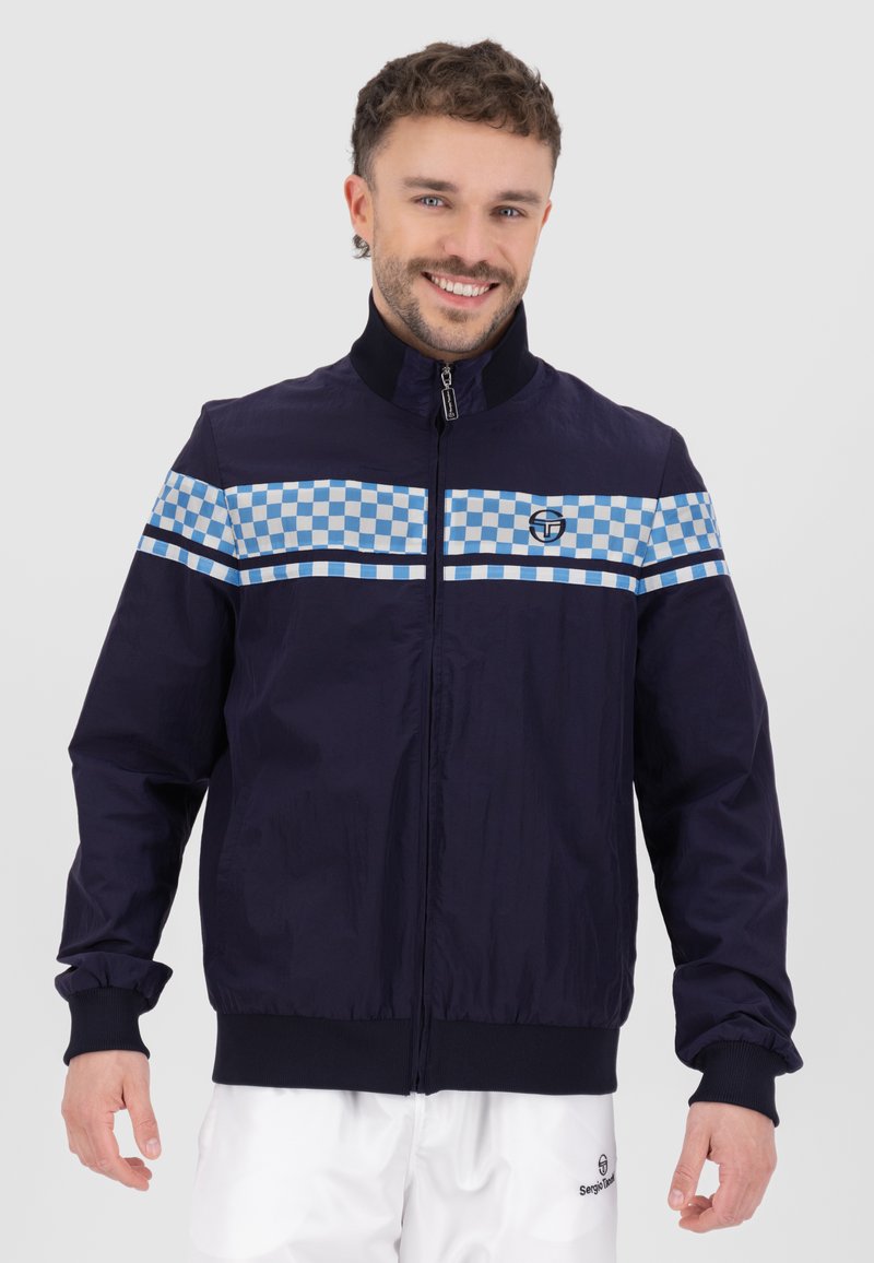 Giacca a vento navy con colletto rialzato, caratterizzata da un motivo a quadretti blu chiaro sul petto e polsini elasticizzati. Logo sul petto.