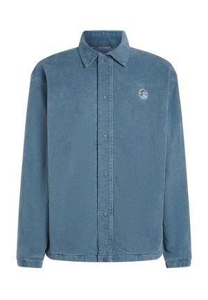 Blue corduroy button-up shirt with long sleeves, featuring a small patch logo on the chest, smooth texture, and standard collar.