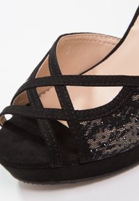 Chaussure à talon noir avec des sangles en daim croisées, des détails en dentelle avec des perles noires et une doublure intérieure lisse. Taille marquée comme 37.