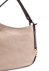 Beige suède schoudertas met een bruine leren schouderband en gouden hardware accent. Beschikt over een glad oppervlak en een gebogen, minimalistisch ontwerp.