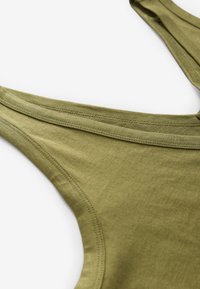 Detailní záběr na spodní díl plavek z olivově zelené látky s propracovaným prošitím na bílém pozadí.