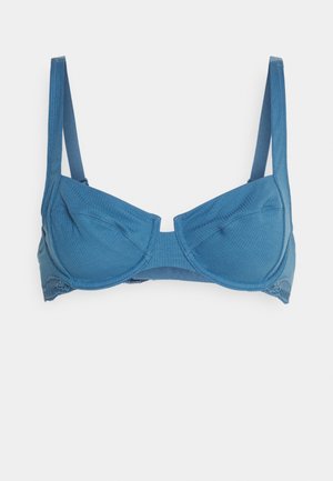 Modra, rebrasta tkaninska modrček z žičnimi košaricami in čipkastim obrobom na dnu, ki ima nastavljive naramnice in brezšivno zasnovo.