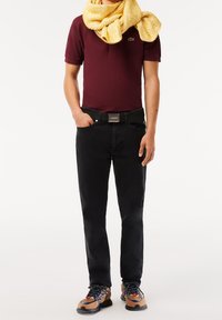 Polo maroon, jeans noirs, écharpe tricotée jaune, ceinture noire avec logo, et baskets multicolores avec des matériaux texturés et des accents de design.