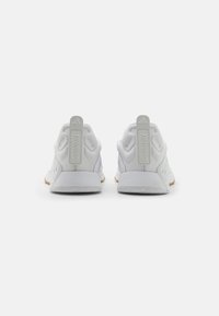 Witte sportieve schoenen met een strak ontwerp, voorzien van textuur aan de zijkanten, een gevoerde hiel en een rubberen loopzool, gelabeld met "TRAINING" op de achterkant.