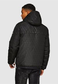 Czarna pikowana kurtka z kapturem, o fakturowanym wzorze w karo i elastycznych mankietach, zestawiona z ciemnymi dżinsami.