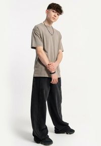 Szara bawełniana koszulka z krótkim rękawem, w połączeniu z luźnymi czarnymi dżinsami. Czarne sneakersy dopełniają swobodny strój. Białe tło.