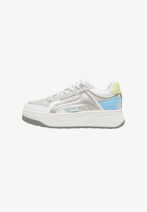 Personne portant des baskets blanches et bleues et une jupe rose debout sur un trottoir à côté d'une porte de voiture ouverte.