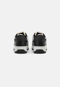 Sneaker neri con tomaia in pelle liscia, suola bianca e collare imbottito. Presentano accenti bianchi a contrasto e una suola in gomma testurizzata.
