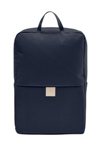 Mochila de tela azul marino con forma cuadrada, asa superior y un parche de logo beige. Textura suave con diseño minimalista.
