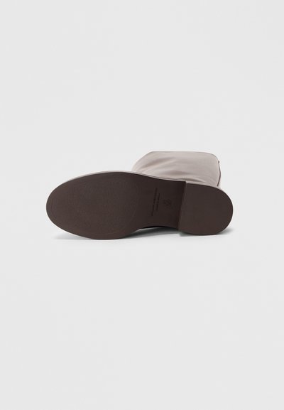 Semelle en caoutchouc marron d'une botte avec une forme lisse et arrondie ; matériau supérieur de couleur neutre claire, sans texture avec des détails de couture minimaux.