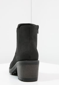 Botín negro de tobillo hecho de un material similar al ante, con un tacón texturizado, que presenta un cierre lateral y un diseño de punta redonda.