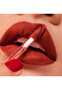 Rossetto liquido opaco applicato con un applicatore a forma di piede di cervo. Il colore delle labbra è rosso intenso con una finitura testurizzata, su pelle chiara.