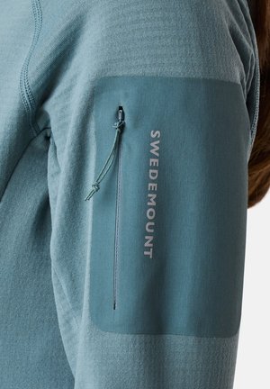Long-sleeve teal sweatshirt features a soft fabric, ribbed texture, and a zippered pocket on the sleeve with "SWEDEMOUNT" branding.