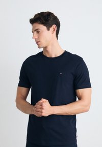Camiseta de algodón azul marino con cuello redondo y mangas cortas; presenta un pequeño logo rojo, blanco y azul en el pecho.