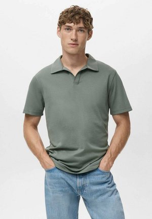 Camisa polo corta verde con cuello, textura suave y un corte moderno, combinada con jeans azul claro. Diseño simple y minimalista.
