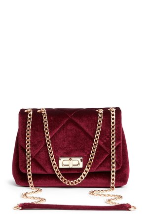 Quiltet burgunderfarvet velourhåndtaske med guldfarvet kædestrop og rektangulær drejelås på hvid baggrund.