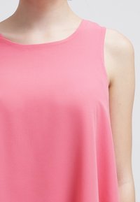 Haut sans manches en tissu rose doux, avec un col rond et une silhouette fluide, une texture lisse sans motifs ni accents visibles.