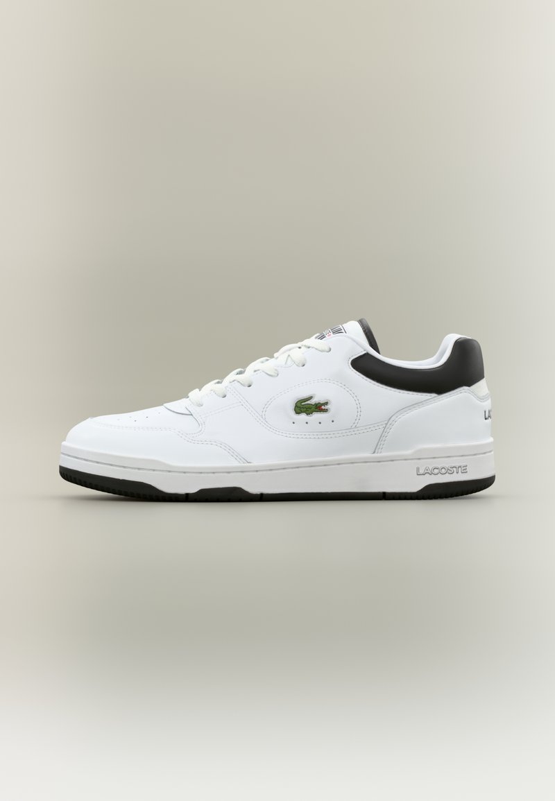 Sapatilha branca de cano baixo da Lacoste com colarinho preto, logótipo de crocodilo verde na lateral e sola preta, apresentada de perfil sobre fundo neutro.