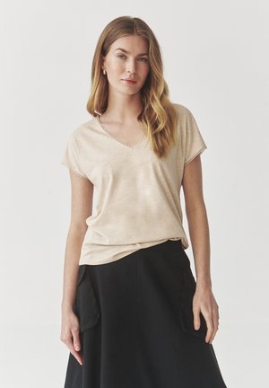 Haut V à manches courtes beige clair avec une coupe décontractée, texture lisse, détails de couture subtils, associé à une jupe noire dotée de poches latérales.