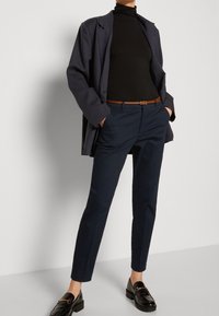 Navy blue tailored trousers with a sleek design, paired with a black turtleneck and a dark jacket, complemented by shiny black loafers.