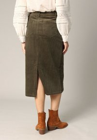 Oliegroene corduroy midi-rok met een rugsplit, gedragen met bruine suède enkellaarsjes en een lichtromige blouse met kantaccenten.