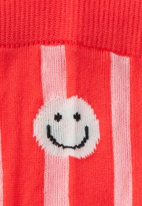 Raudonos dryžuotos kojinės su besikeičiančiais rožiniais ir raudonais vertikaliais dryželiais. Su balto ski pavidalo šypsenėlės logotipu juodais akcentais. Minkšta mezgimo tekstūra.