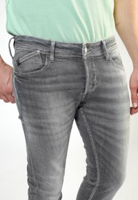 Grå denimjeans med slim fit, som har en femfickdesign, bälteshögar och dragkedja. Tyget har en liten struktur.