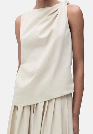 Sleeveless cream top with a draped front and a knotted detail at one shoulder. Fabric appears smooth with a subtle sheen.