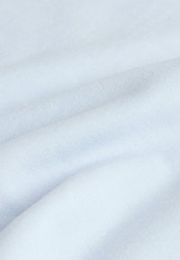 Tissu blanc doux avec une texture de tissage fin visible et des plis délicats créant des ombres et des reflets subtils.