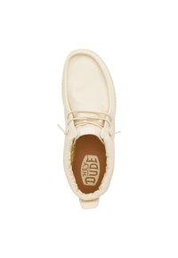 Zapato slip-on de lona beige con puntera redondeada, cordones elásticos y plantilla marrón con el logo "HEY DUDE". Detalle de costura texturizada.
