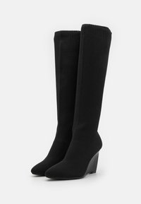 Bottes noires à talons wedges, hauteur genoux, avec un dessus en tricot texturé et un design à bout pointu. Talon rembourré pour un confort accru, silhouette élégante et moderne.