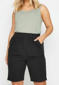 Svarta shorts med elastisk midja och sidofickor, kombinerade med en ljusgrön ärmlös topp, som framhäver en avslappnad passform och en jämn tygstruktur.