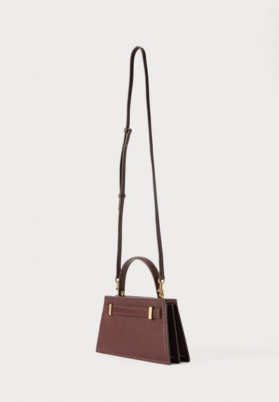 Malá tmavě hnědá kožená kabelka s horní rukojetí, zlatou hardware a nastavovacím dlouhým popruhem, stojící na bílém pozadí.
