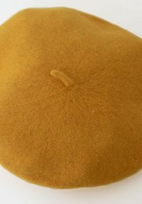 Beret jaune moutarde en laine douce, de forme ronde, texture lisse, avec un petit détail en boucle au centre supérieur.