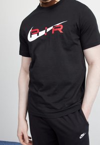 Svart bomullströja med en stor vit och röd "AIR" grafisk design över bröstet. Kort ärm och rundad halsringning.