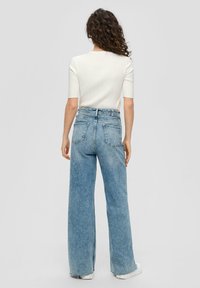 Lichte witte geribbelde top met korte mouwen, gecombineerd met hoge taille, wijde lichtblauwe denim jeans met achterzakken en een klassieke snit.