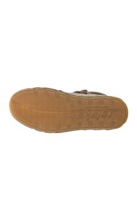 Semelle de chaussure Skechers, avec une construction en caoutchouc texturé. Couleur beige avec des rainures de traction et un logo sur le côté.