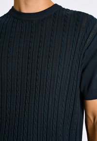 Granatowa, dziana bluzka z krótkim rękawem, z teksturą prążkową, wzorem w warkocze oraz okrągłym dekoltem. Wykonana z miękkiego, oddychającego materiału.