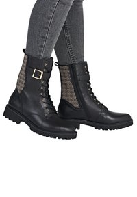 Bottines en cuir noir avec un panneau en textile à motifs, des accessoires dorés, un laçage à l'avant et une fermeture éclair sur le côté, dotées d'une semelle en caoutchouc épaisse.