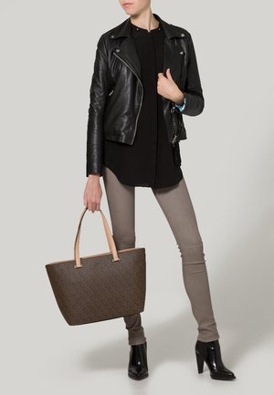 Borsa a tracolla marrone con motivo, manici rosa chiaro, abbinata con una giacca di pelle nera, top nero e pantaloni skinny grigi. Stivali neri con tacco.