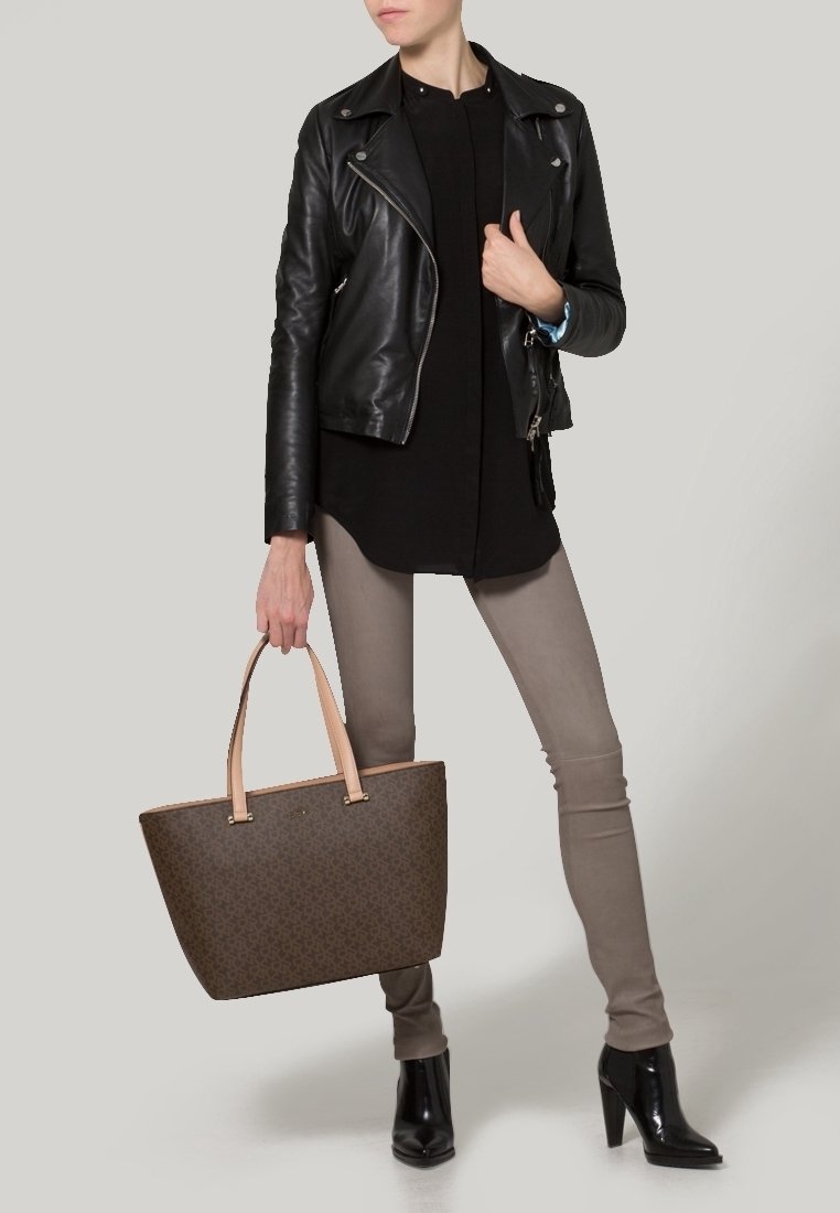 Brun mönstrad tote-väska med ljusrosa handtag, tillsammans med en svart läderjacka, svart topp och grå smala byxor. Svarta klackboots.