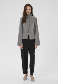 Grå lynlåsjakke med høj krave, lange klokkeærmer og en tekstureret stof. Sammen med sorte bukser og beige hæle.