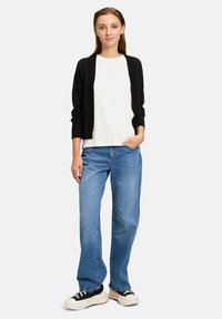 Svart cardigan över en vit t-shirt, tillsammans med ljusblå raka jeans och svarta sneakers med vita sulor och röda detaljer.