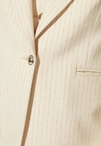Beige blazer med vertikal guldstribet mønster, enkeltknap design, metal knapper og en brystlomme for et skræddersyet look.