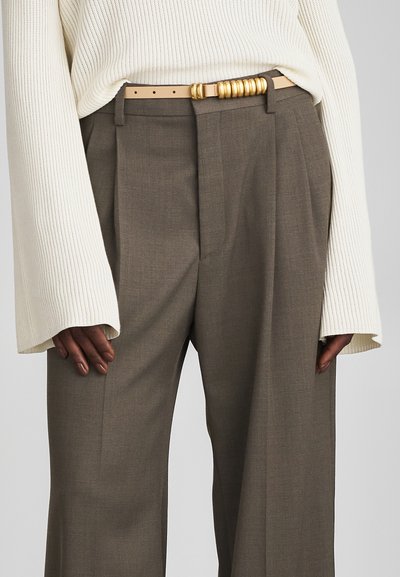 Pantalons marron ajustés à coupe droite, en tissu texturé, associés à un pull en crème à côtes et une ceinture beige avec des accents dorés.