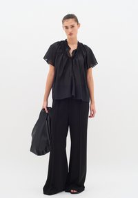 Blusa nera a maniche corte con scollo arricciato, abbinata a pantaloni neri larghi e una borsa nera testurizzata. Tessuto liscio, design minimal.