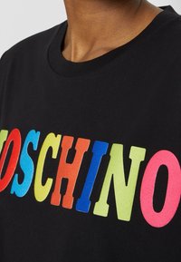 Zwart T-shirt met ronde hals en grote, kleurrijke blokletters die "MOSCHINO" op de borst spellen.